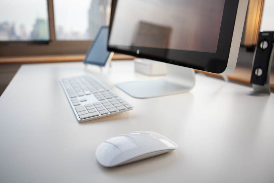 Poste de travail avec écran, clavier et souris posés sur un bureau blanc devant une fenêtre